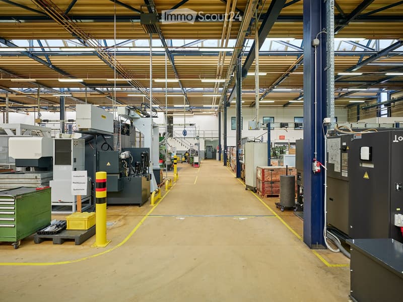 Industrial building with large open space, industrial machines, yellow and red poles, green storage boxes, and metal beams