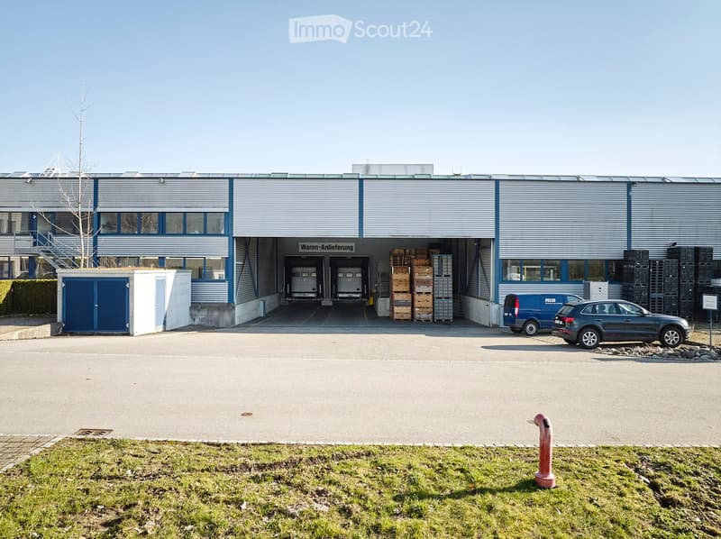 Warehouse building with loading bay, blue doors, two cars parked, and a fire hydrant