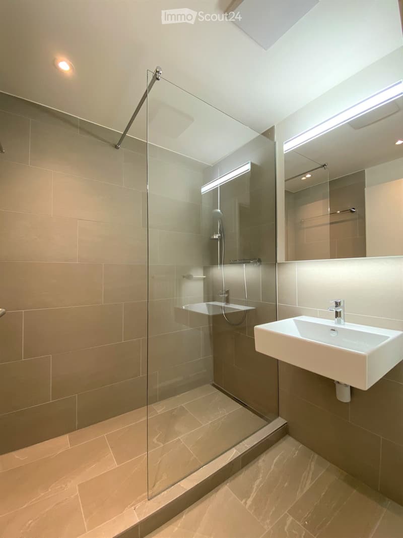 modern bathroom with glass shower enclosure, white sink, beige tiles, mirror, shower head, and towel rack