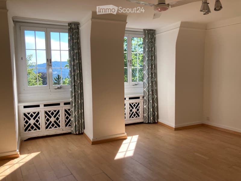 Empty room with wooden flooring, large windows with curtains, and a white cabinet with decorative lattice panels.