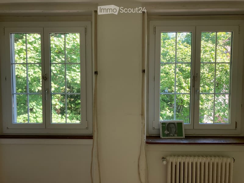Empty room with two windows, radiator, and a small framed picture on the windowsill.