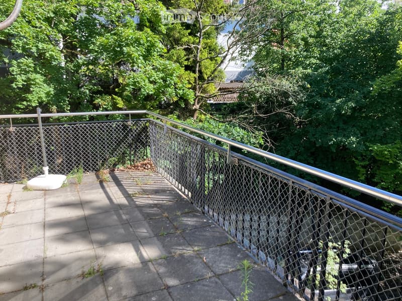 A narrow outdoor staircase with metal railings and a chain-link fence, surrounded by greenery and trees.