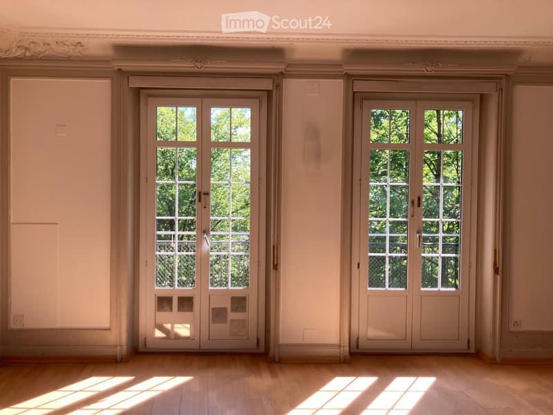 Empty room with wooden flooring, large double doors with glass panels, and natural light streaming in.