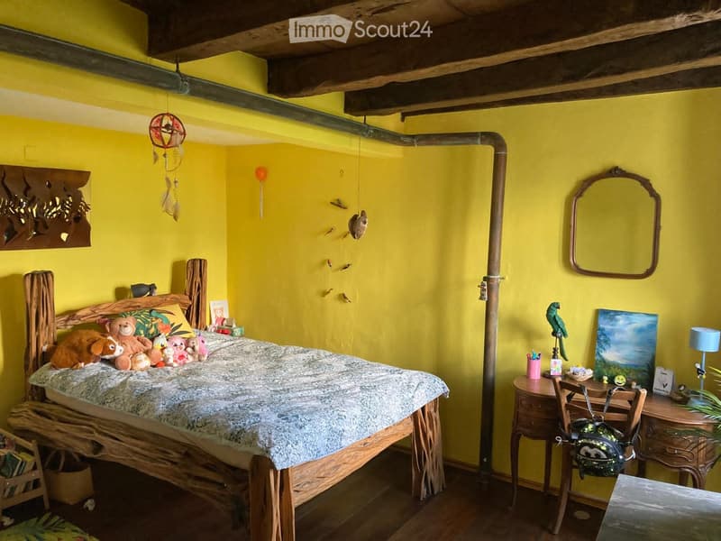 A bedroom with a wooden bed, yellow walls, wooden desk, mirror, lamp, and various decorative items.