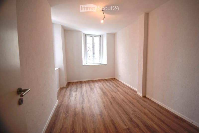 Empty room with wooden floor, white walls, a window, and a door.