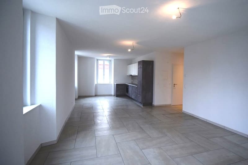Empty room with white walls, tiled floor, kitchen area with cabinets and a window