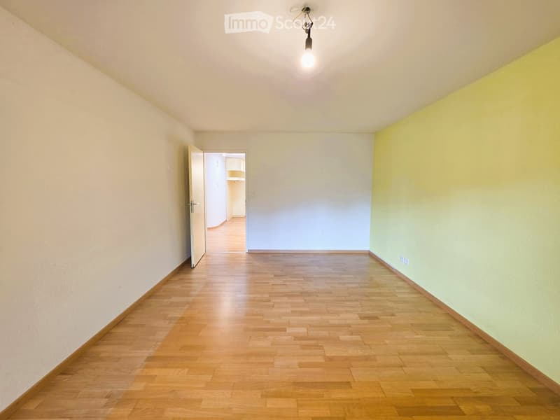 Empty hallway with wooden flooring, white walls, and a single hanging light fixture. Open doors lead to adjacent rooms.