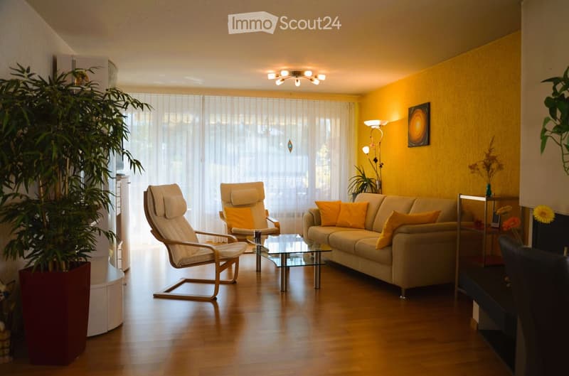 Living room with beige sofa, glass coffee table, two armchairs, yellow walls, floor lamp, potted plants, and a window with white curtains.