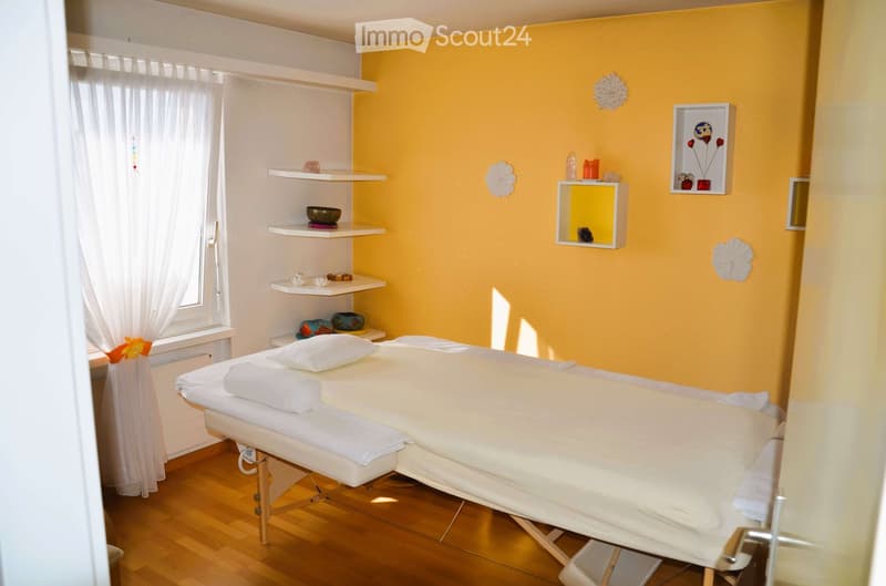 massage table, white sheets, pillows, shelves with decorative items, yellow wall, white curtains