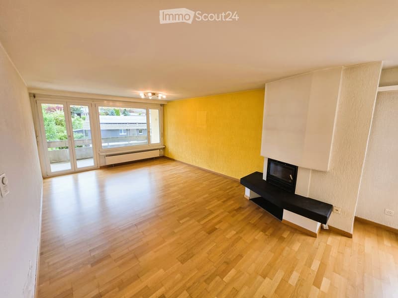 Empty room with wooden flooring, fireplace, large windows, and sliding glass doors leading to a balcony.