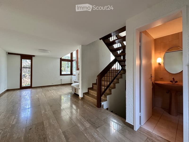 Empty room with wooden floor, white walls, wooden staircase, and a sink with a mirror in the corner.