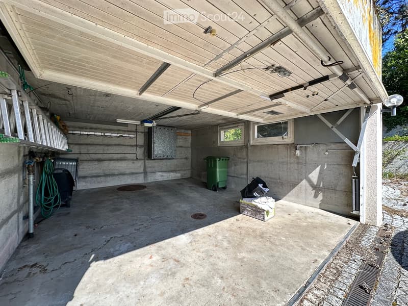 empty garage with concrete floor, metal beams, two windows, two trash bins, and a ladder