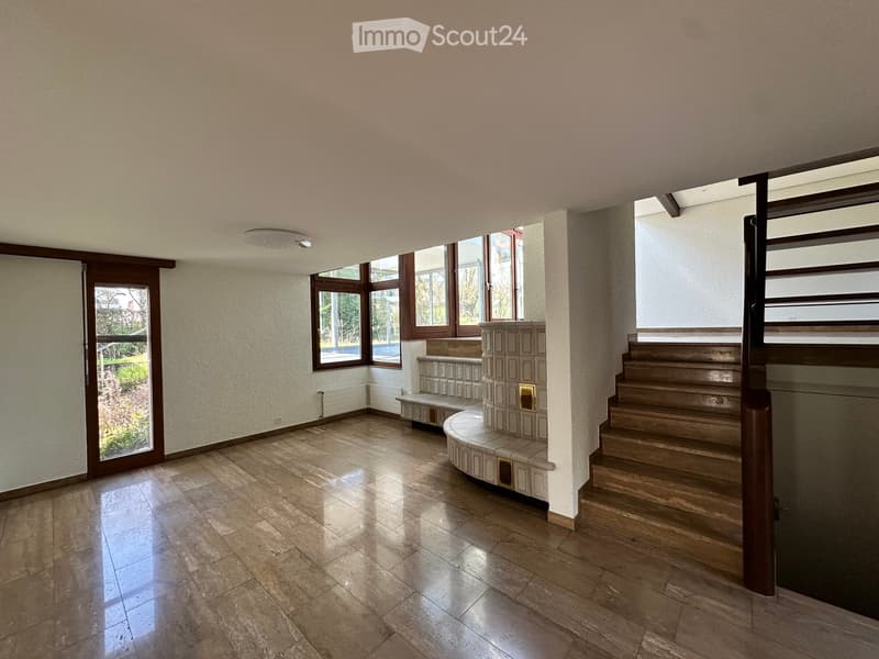 Empty room with wooden floor, white walls, large windows, wooden stairs, and a bench