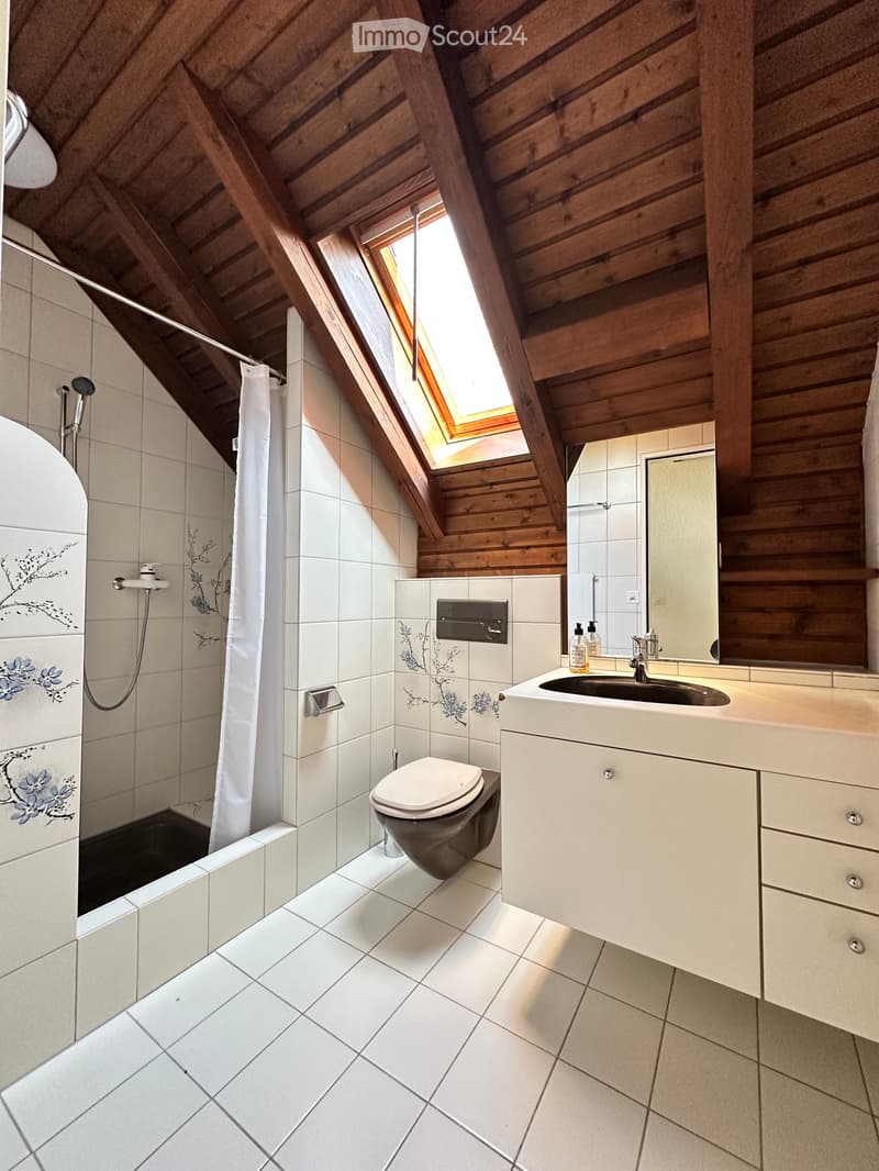 Bathroom with white tiles, wooden ceiling, shower, toilet, sink, mirror, and skylight