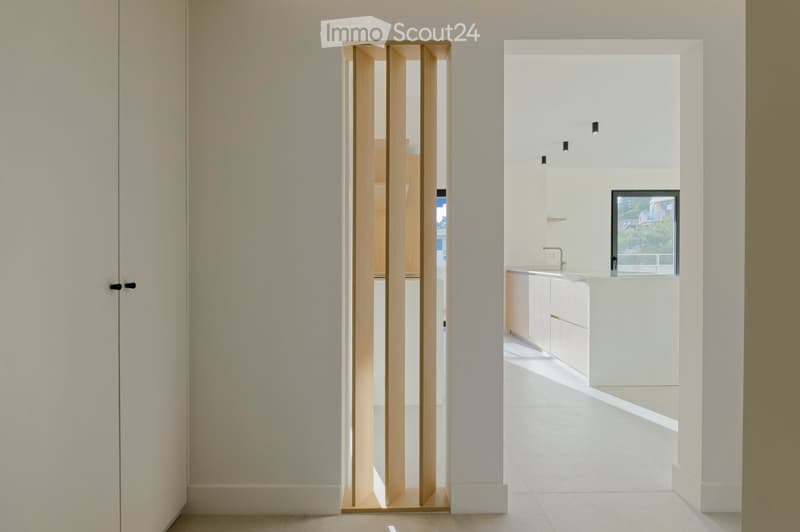 minimalist room, white walls, wooden door, white flooring, open to kitchen