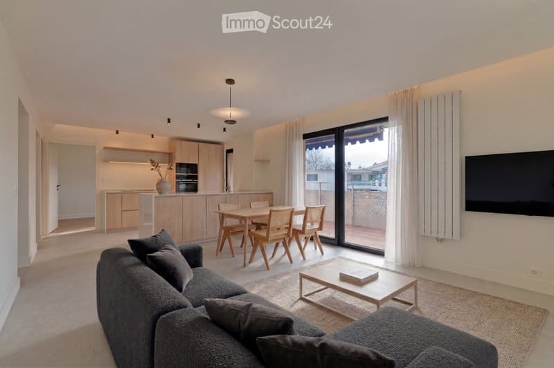 modern living room with large windows, wooden dining table, gray sofa, wooden coffee table, TV, wooden floor, kitchen area