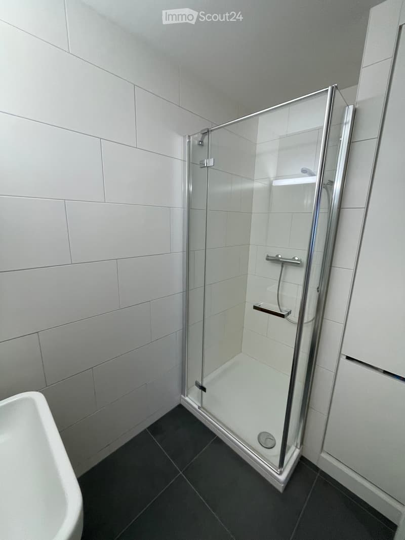 modern bathroom with white tiles, glass shower enclosure, white sink, black floor