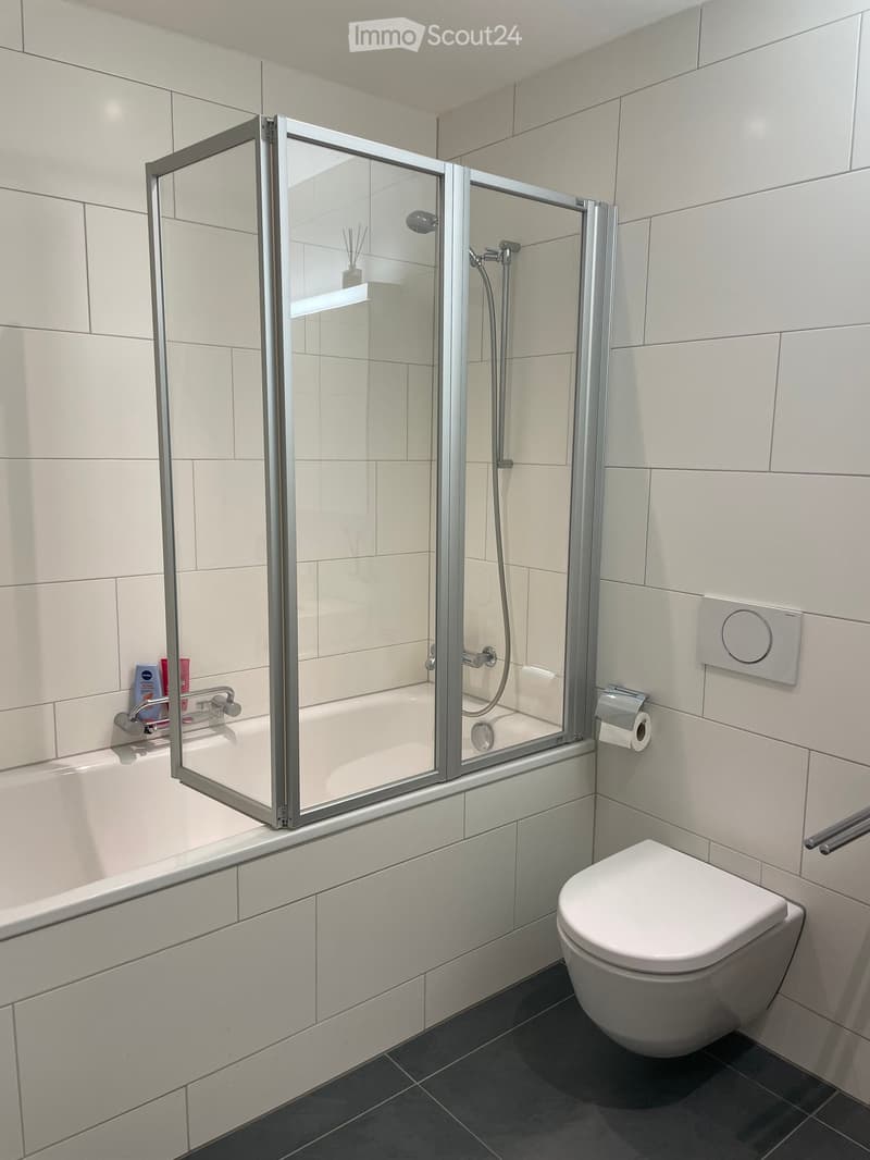 modern bathroom with white tiles, bathtub, shower, toilet, and a toilet paper holder