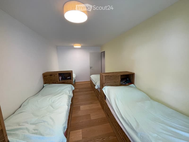 Two single beds, wooden headboards, white bedding, wooden floor, white walls, ceiling lights