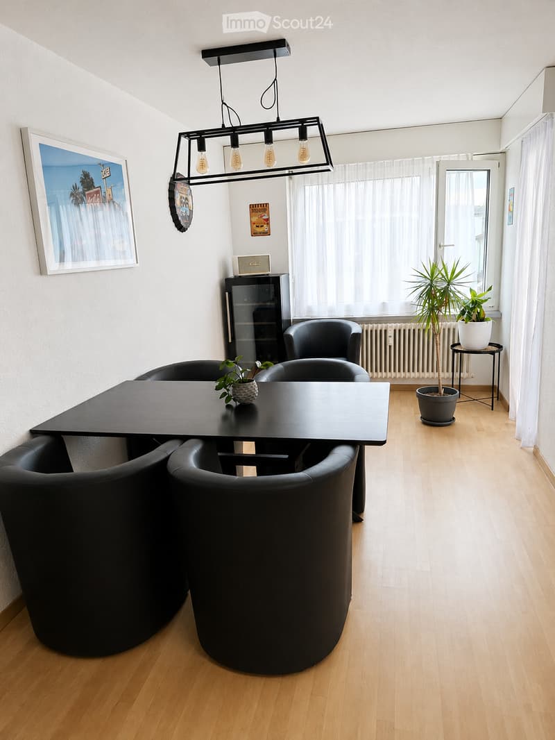 Dining area with a black table and four black chairs, a picture frame on the wall, a black cabinet, a radiator, a potted plant, and a chandelier