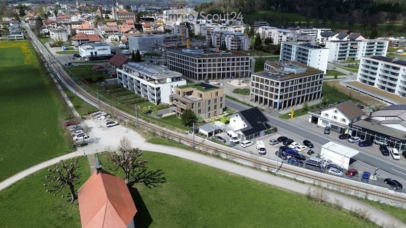 Aerial view of a town with multiple buildings, some under construction, green spaces, and a railway track.