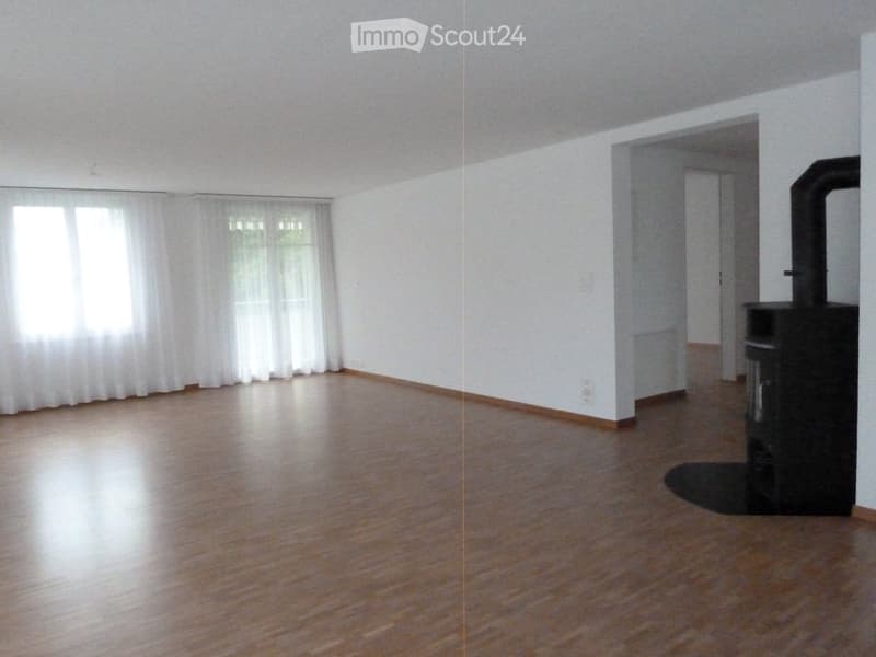 Empty room with wooden flooring, white walls, large windows with white curtains, and a doorway leading to another room.