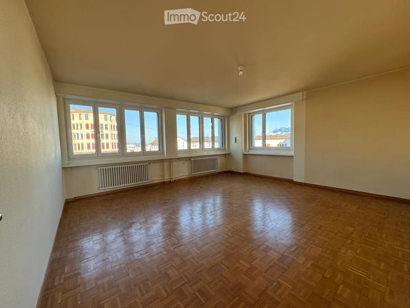 Empty room with wooden floor, large windows, white walls, radiators, and a ceiling lamp