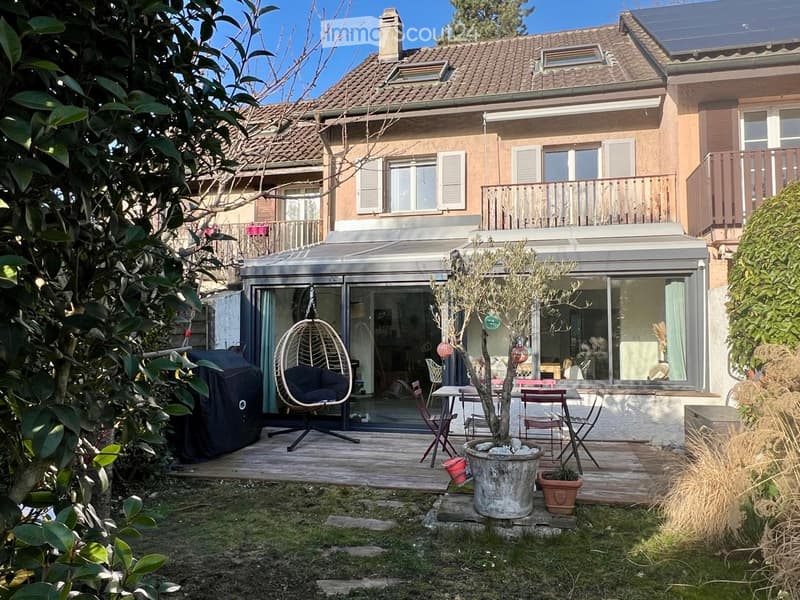 2 story house, brown roof, glass doors, wooden deck, outdoor table and chairs, hanging chair, tree, solar panels