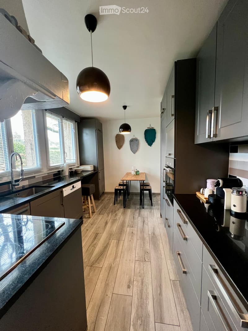 modern kitchen with wooden floor, black countertops, gray cabinets, pendant lights, sink with faucet, dining table with chairs, appliances, and decorative items