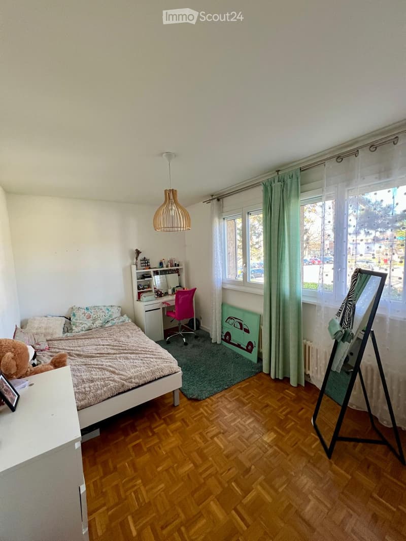Bedroom with bed, desk, chair, rug, and various items on the desk and bed