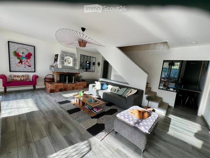 Living room with fireplace, gray sofa, coffee table, rug, pink chair, wooden floor, staircase, mirror, picture frame, decorative items