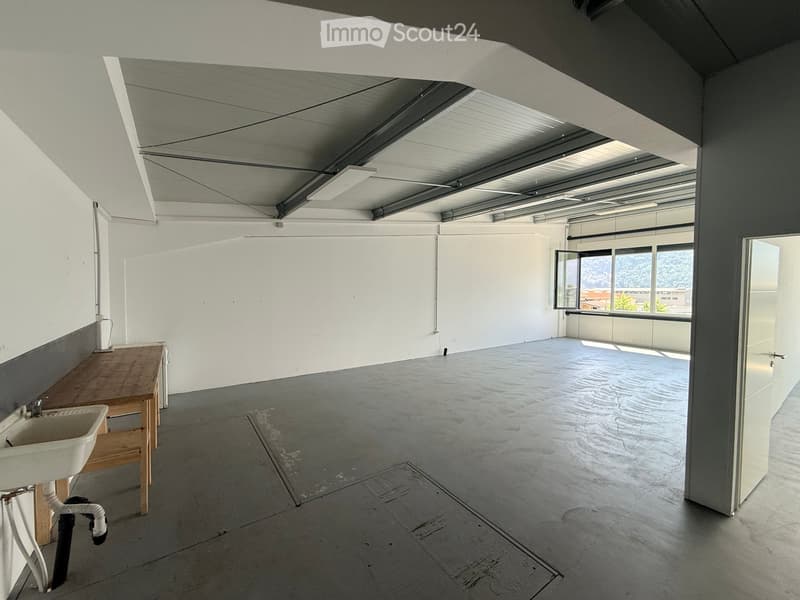 Minimalist room with concrete floor, white walls, a sink, and a wooden bench. Large windows provide natural light and a view of the outside.