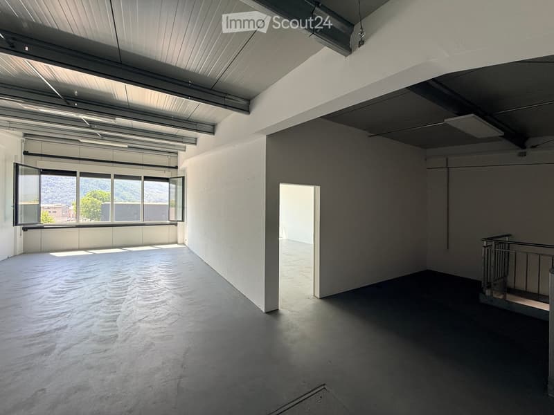 Empty room with bare walls, concrete floor, large windows, and a staircase leading to another level.
