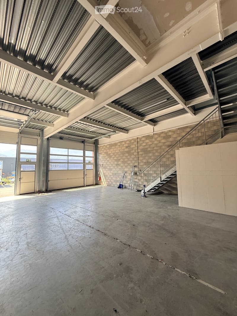 Empty warehouse space with concrete floor, metal staircase, large garage doors, and minimal equipment.