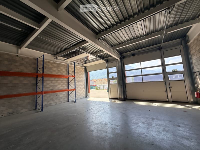 Empty garage with concrete floor, metal shelving units, large garage doors, and natural light from windows.
