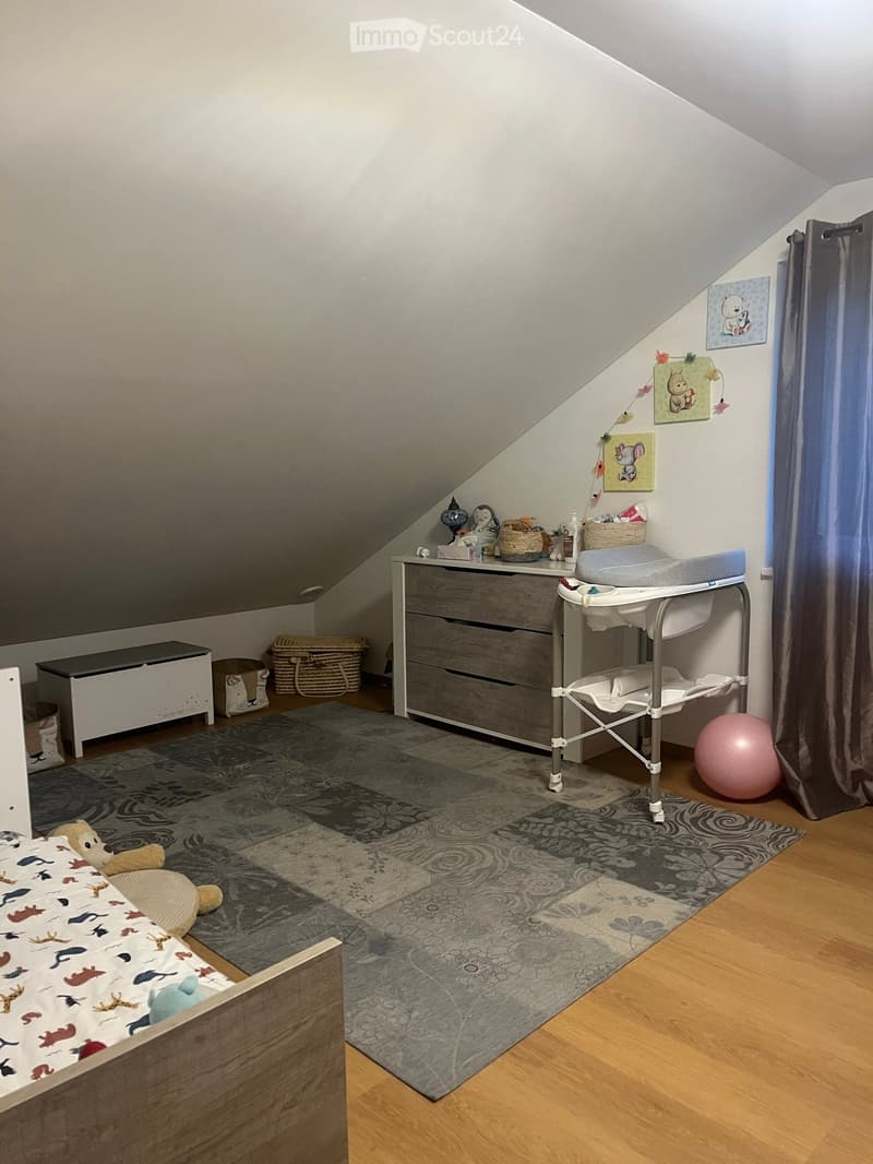 A child's bedroom with a bed, a rug, a changing table, a storage box, a basket, and a pink ball.