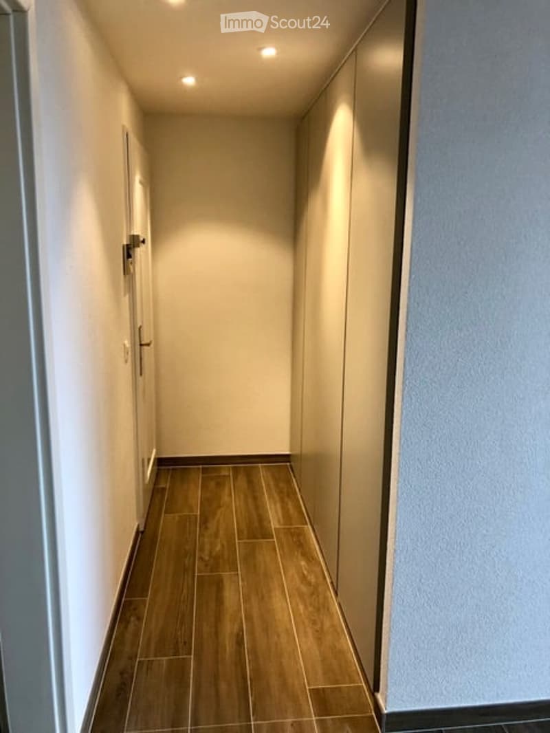 Empty hallway with wooden floor, white walls, and ceiling lights