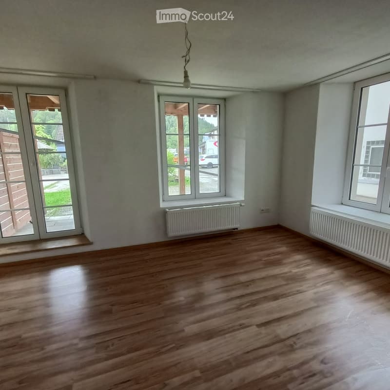 Empty room with wooden flooring, white walls, large windows, and radiators. No furniture or equipment present.