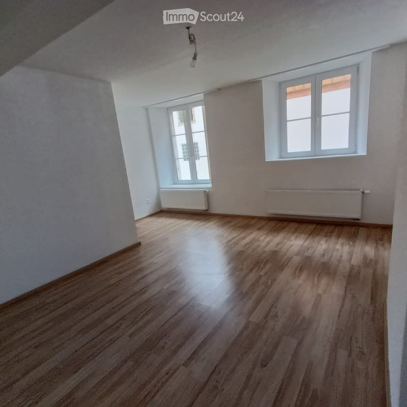 Empty room with wooden flooring, white walls, and two windows with white frames. Radiators are present under the windows.