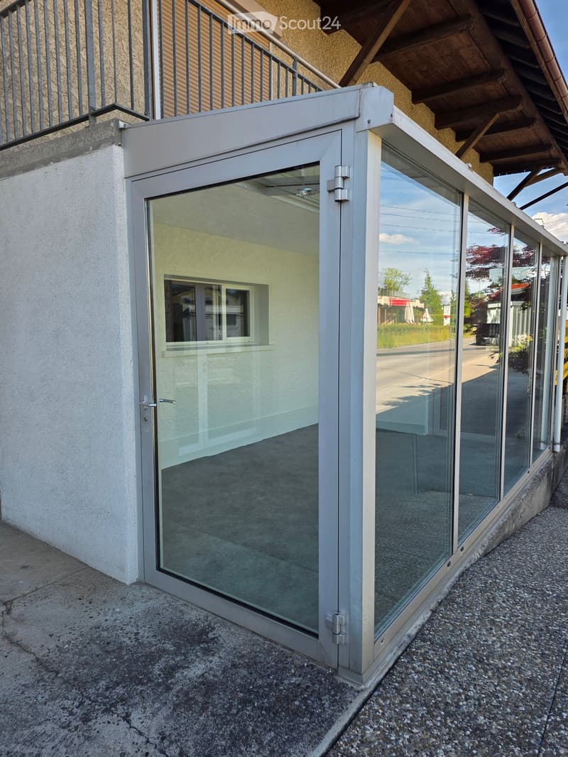 Modern glass balcony with sliding doors, white frame, and metal railing attached to a building.