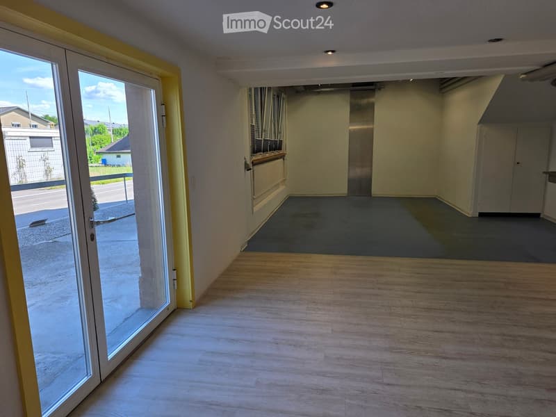 Empty room with wooden flooring, large sliding glass door leading outside, and a view of the street.