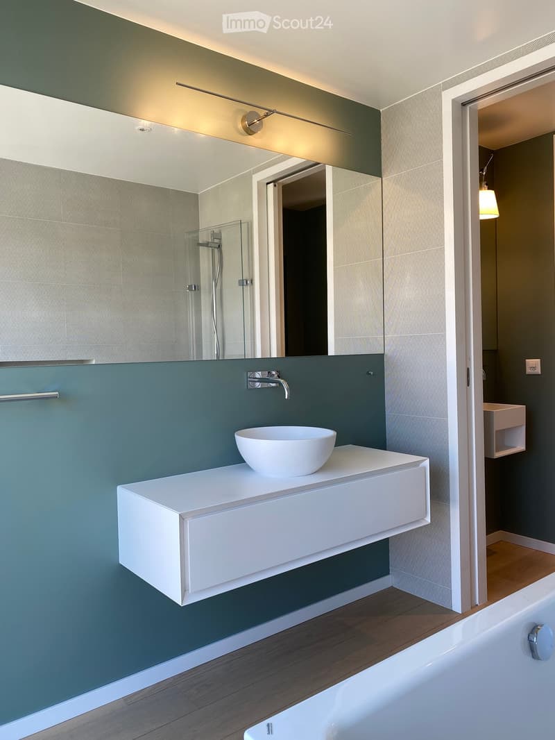 modern bathroom with white bathtub, white sink, large mirror, green wall, wooden floor