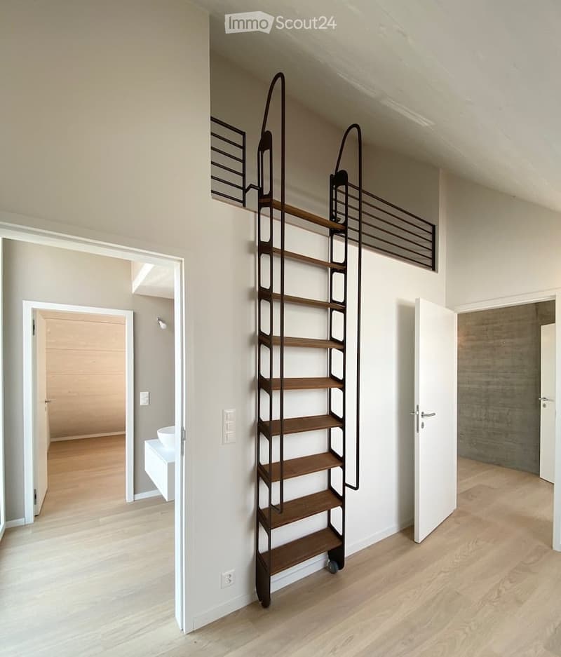 A modern hallway with a sleek, black metal staircase featuring wooden steps, leading to an upper level. The hallway has light-colored walls, wooden flooring, and several open doors leading to other rooms.