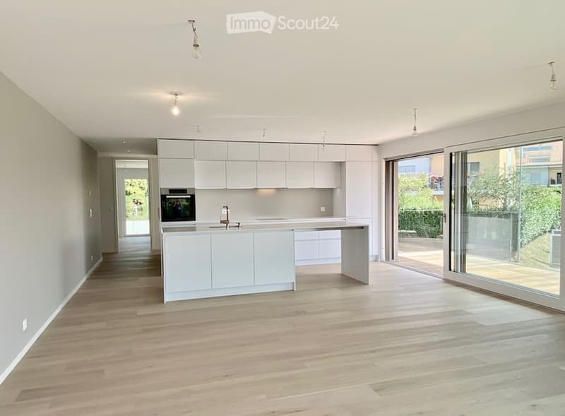 Modern, minimalist kitchen with white cabinets, a central island, and a large glass balcony door leading to an outdoor area.