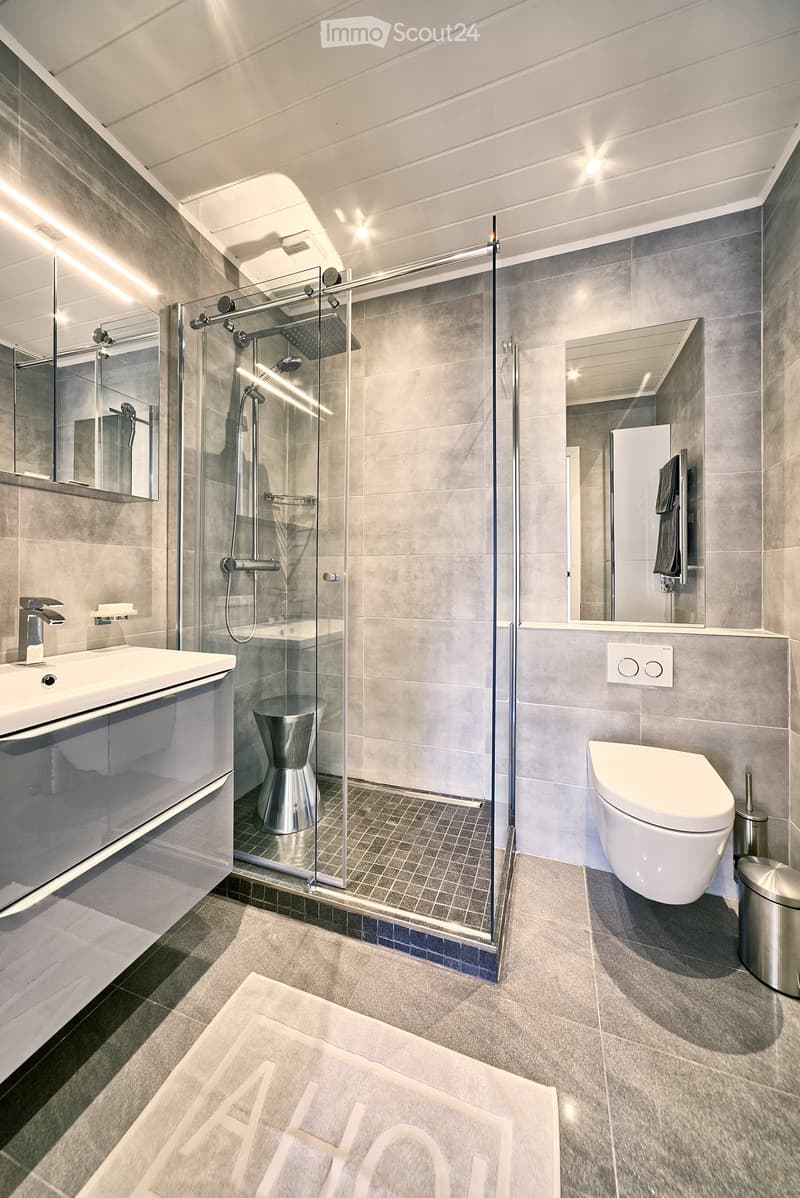 modern bathroom with glass shower, white sink, white toilet, gray tiles, silver fixtures