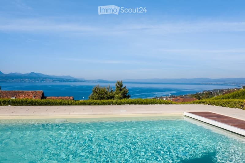 Outdoor swimming pool, wooden deck, manicured lawn, hedges, distant houses, mountains, and sea