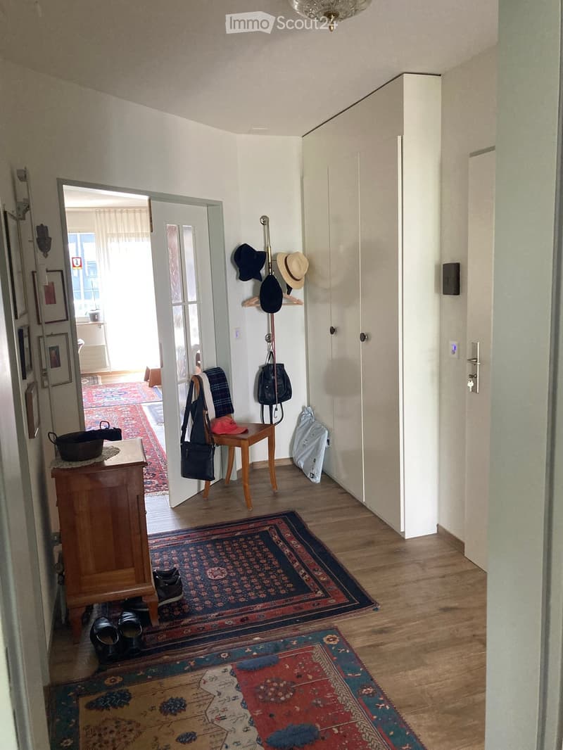 Entrance hall with wooden floor, white walls, wooden cabinet, coat rack, hats, bags, and shoes on the floor, and a chandelier