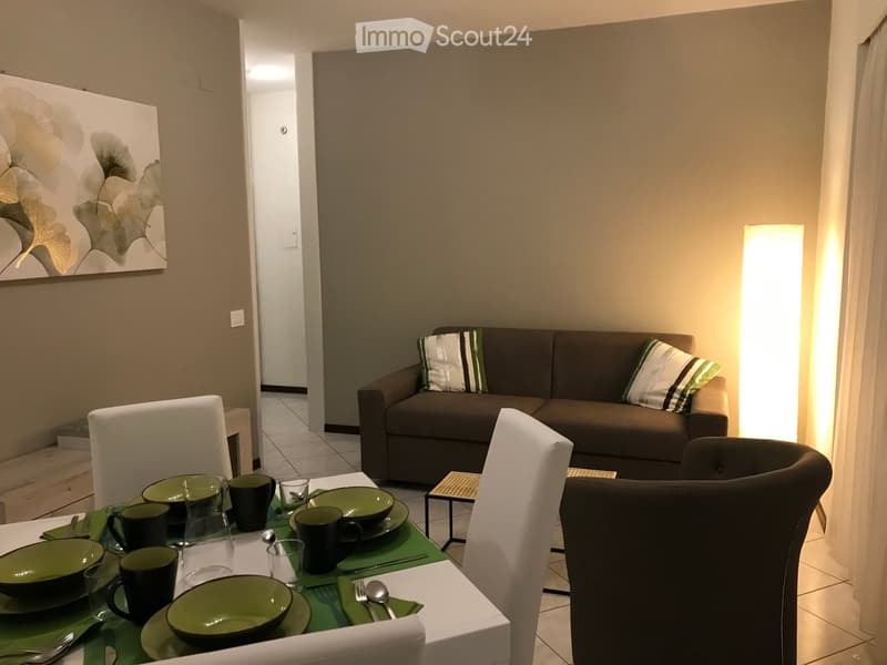 Dining area with a table and chairs, a couch with pillows, a painting on the wall, and a lamp
