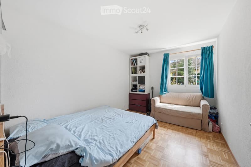 single bed, couch, bookshelf, wooden floor, white walls, window with blue curtains