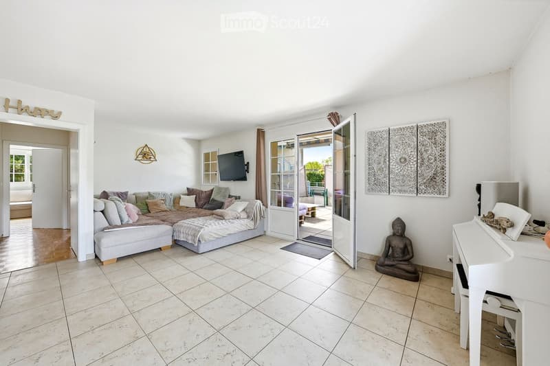 modern living room with white walls, tile flooring, large sofa, TV, open door to balcony, white piano, decorative items